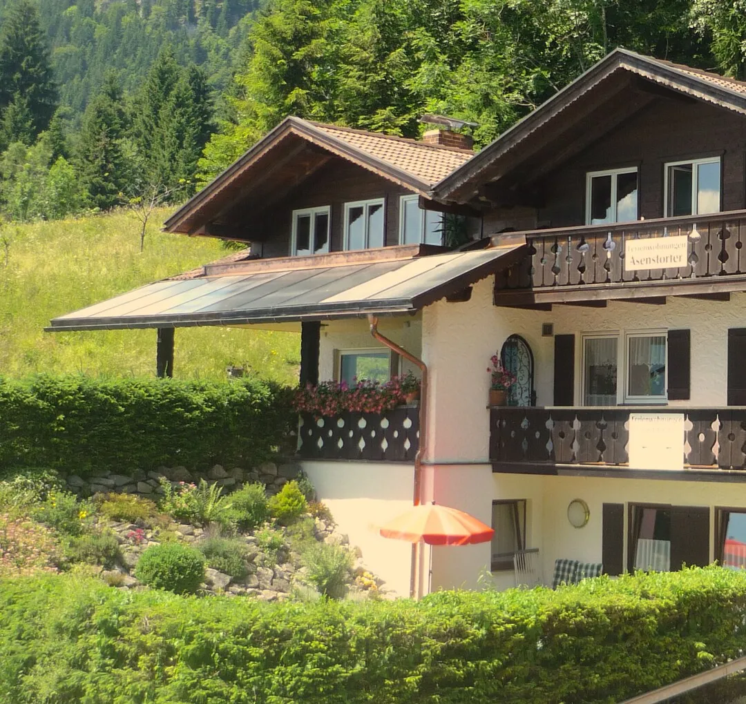 Echtes Foto vom Haus Asenstorfer: Balkone aus dunklem Holz mit Geranien, Schild Ferienwohnungen Asenstorfer