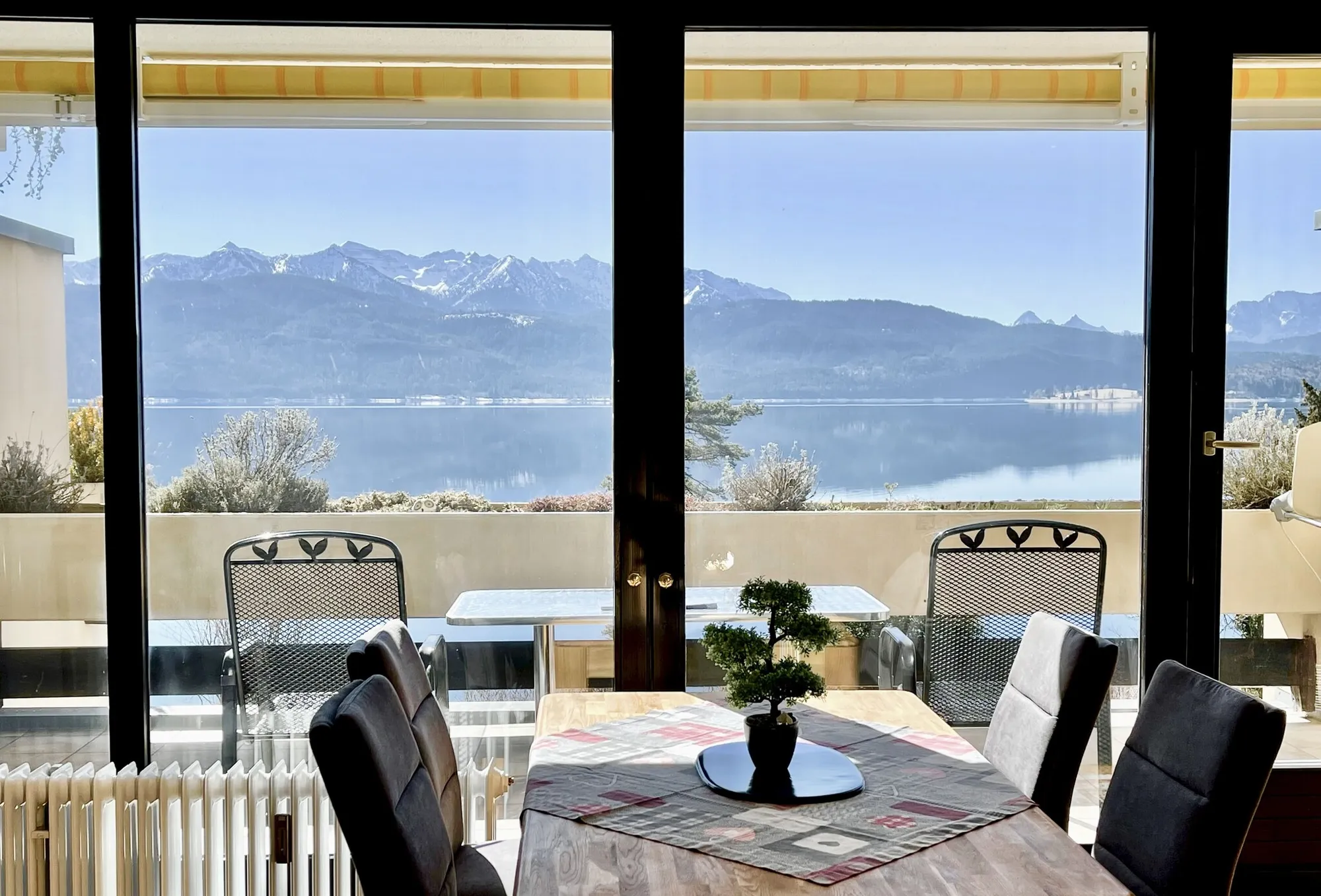 Echtes Foto aus dem Haus Seewinkel: Esstisch vor einer Glasfront, dahinter Balkon, See und Berge
